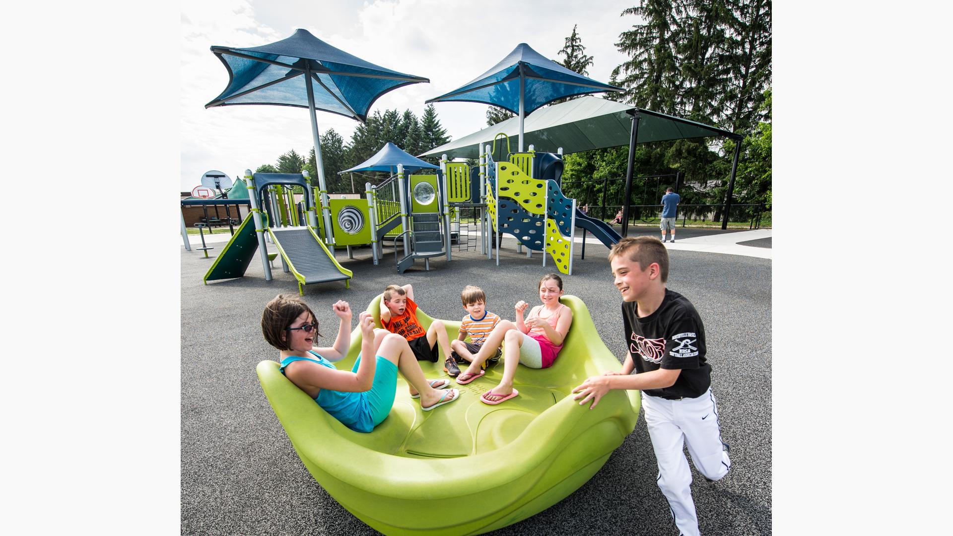 Boy in baseball uniform pushing friends on OmniSpin® Spinner