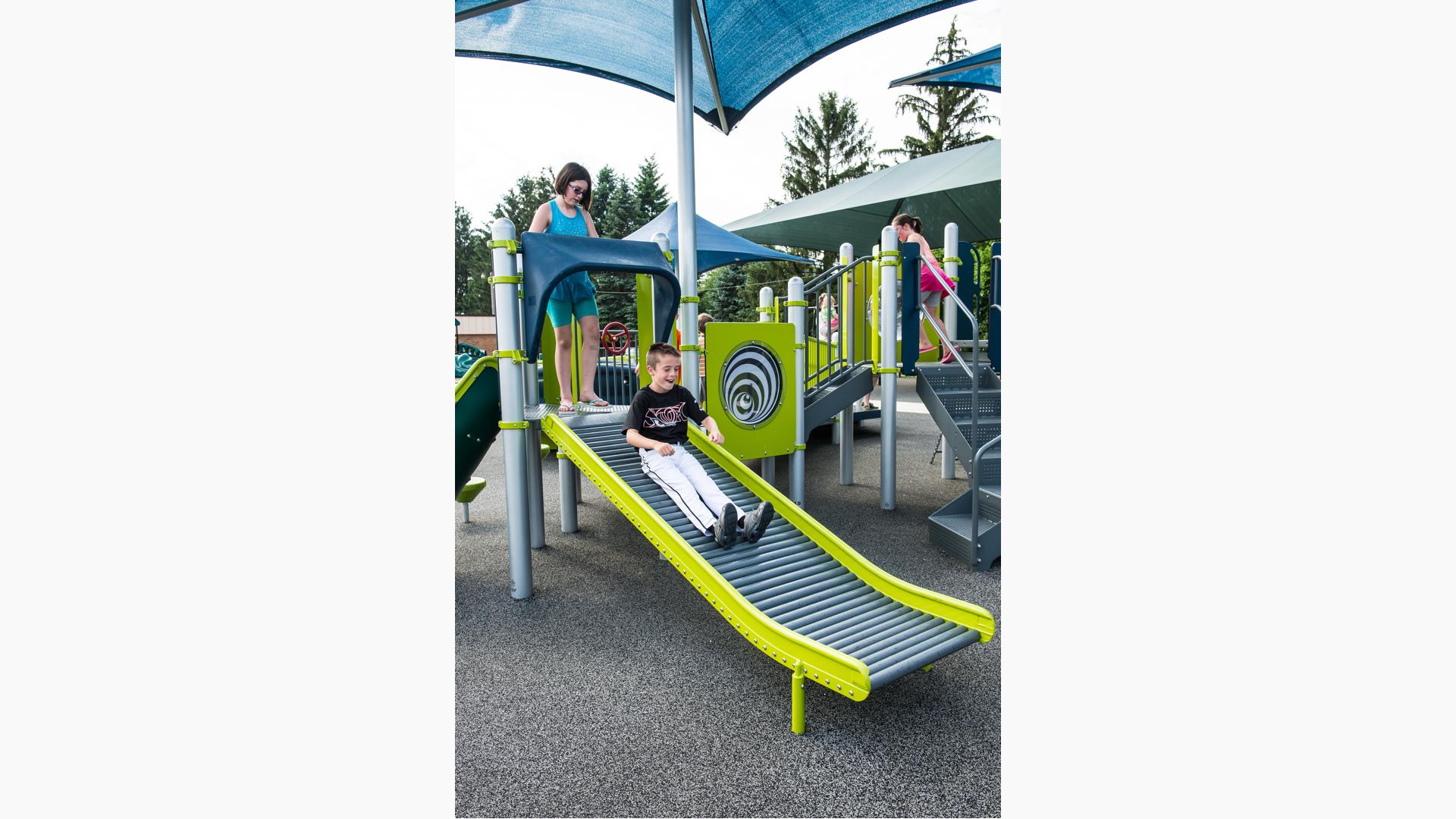 Boy in baseball uniform laughing riding down Roller Slide