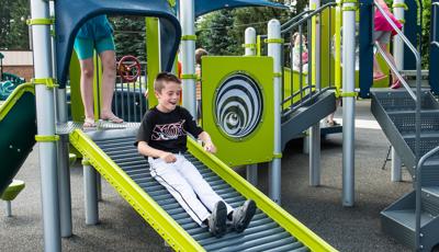 Boy in baseball uniform laughing riding down Roller Slide