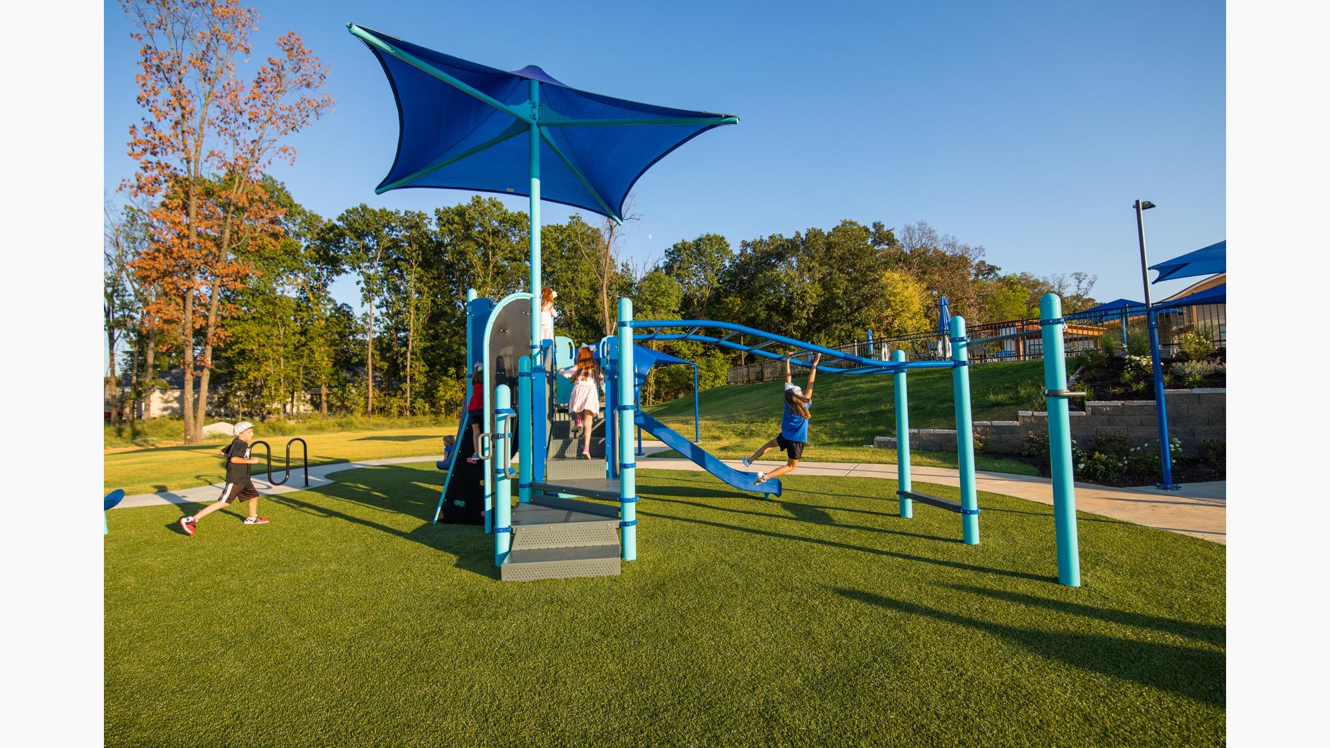 Kids playing on Scissortail Park playground. A girl swinging on overhead events as a boy runs toward play structure.