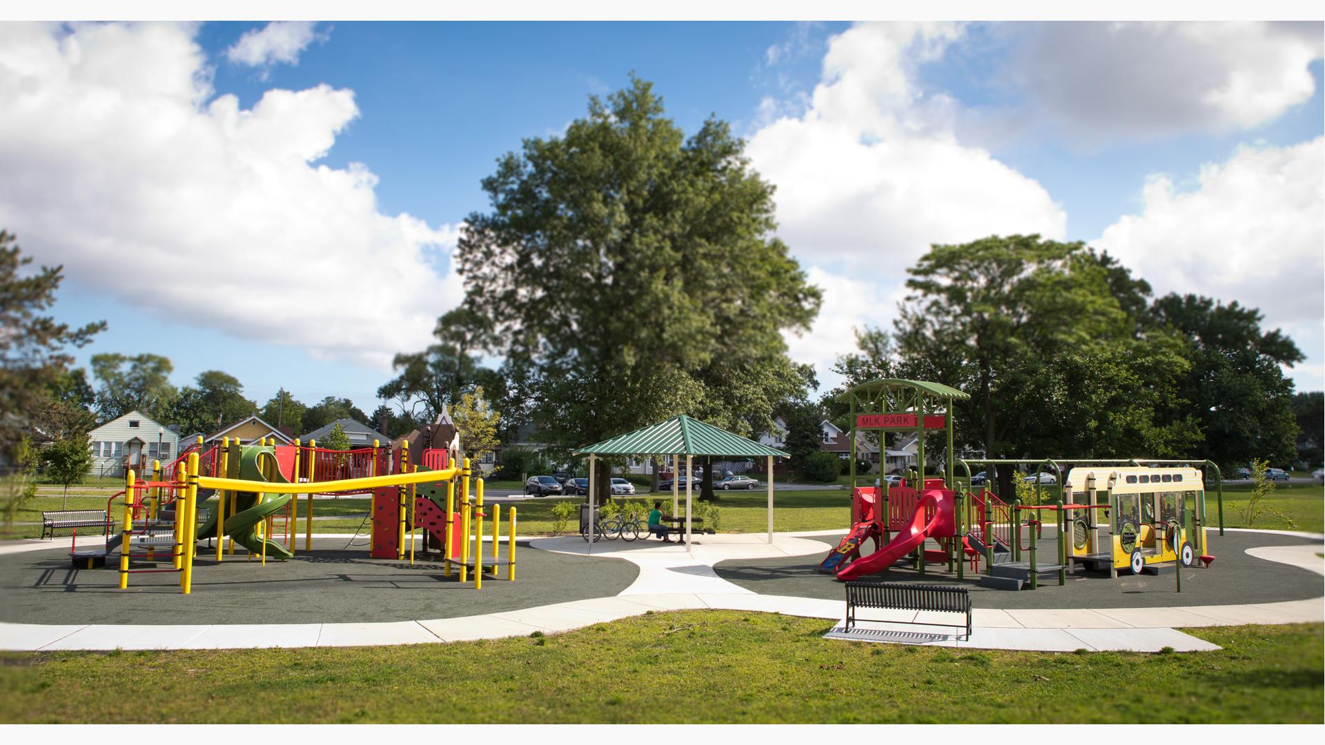 Two playground structures that memorializes Martin Luther King, Jr. are colored in green, red and yellow. A small pavilion sits provides shade to a picnic table between the two play structures.