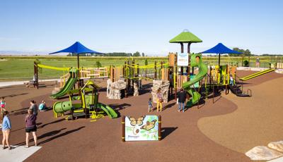 Children and families playing on nature-inspired playground with green slides, bridges, climbing rocks and with interactive panels about the animal life in Idaho. 