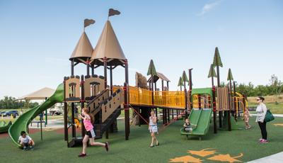 A castle-themed play structure  in a custom fantasy-themed playground, kids are riding slides, and can access ramps, making it accessible for children of all abilities.