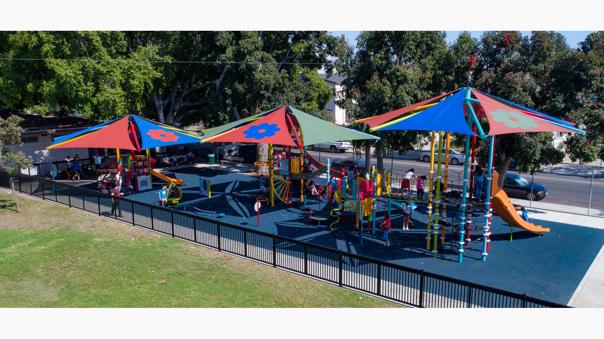 Lincoln Heights Recreation Center, Los Angeles, CA, a festive color scheme along with custom flower-printed SkyWays® shade sails.  Picado banner climbers, sugar skull steppers and DigiFuse® flowers.