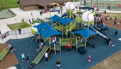 Lots of families playing on an inclusive, fully-ramped and accessible playground with four blue shade structures and two baseball roofs.