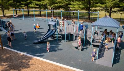 A park playground with two play structures and a long line of swing set bays in the background. Children play all over the larger play structure in the foreground.  