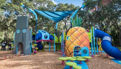 A custom playground designed like the cartoon character Sponge Bob SquarePants pineapple home and his neighbor Squidward’s Easter Island Head home connected by climbers and bridges and other play activities.  